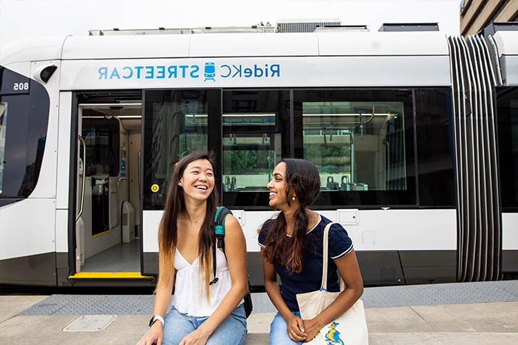 Two smiling students sit in front of the KC Streetcar