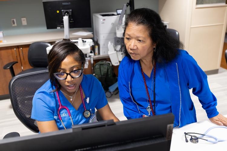 Tatyana Charles and a nurse look at a computer screen, conversing at a nurse's station at University Health